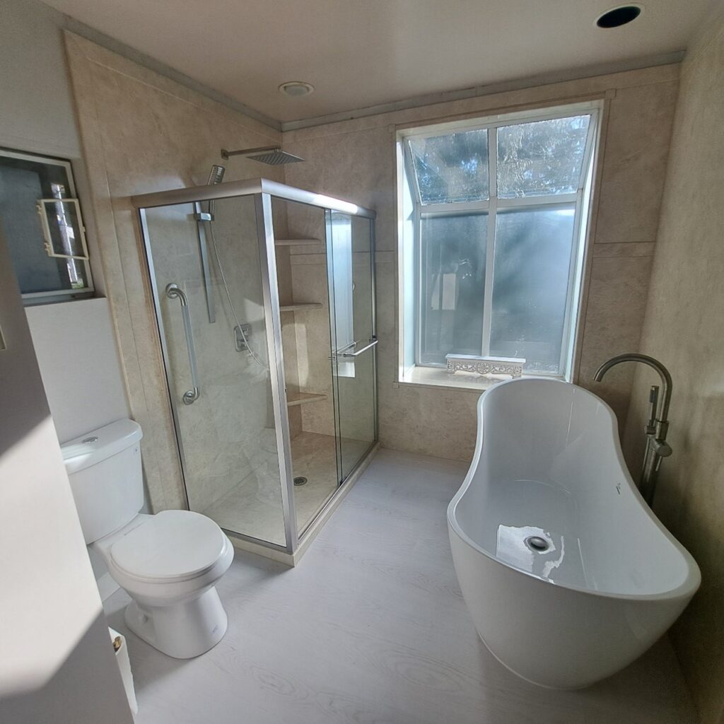 Modern bathroom with a glass shower enclosure, Sentrel bath walls, toilet, and large window letting in natural light. Bathroom remodeling and renovation from Oasis Bath Solutions of Kent Washington